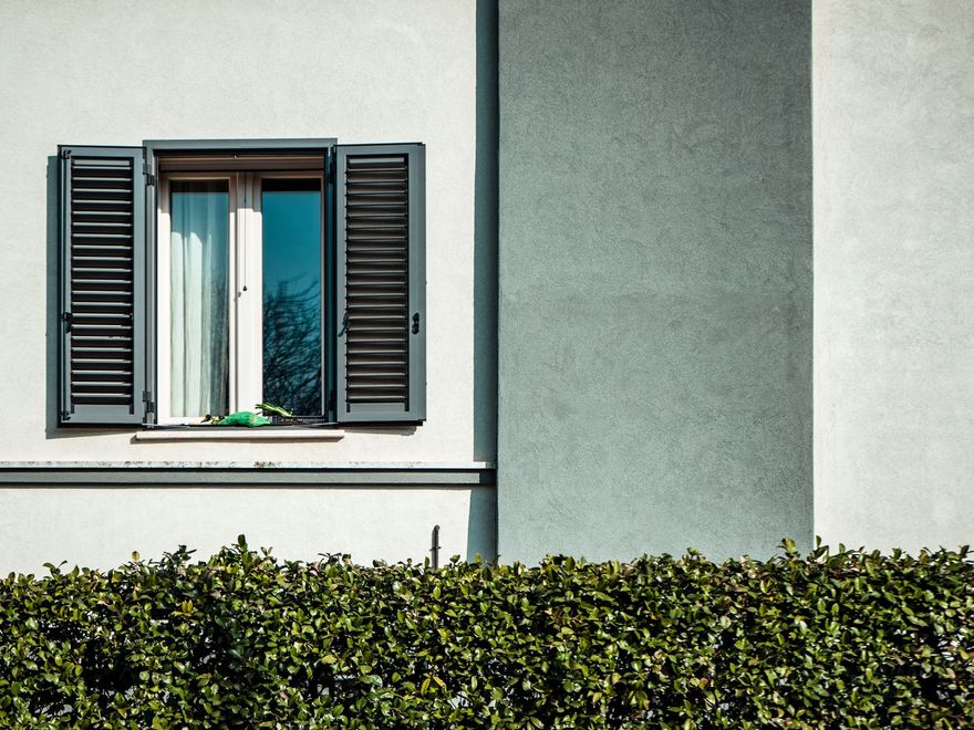 A freshly cleaned window with shutters above a neatly clipped hedge