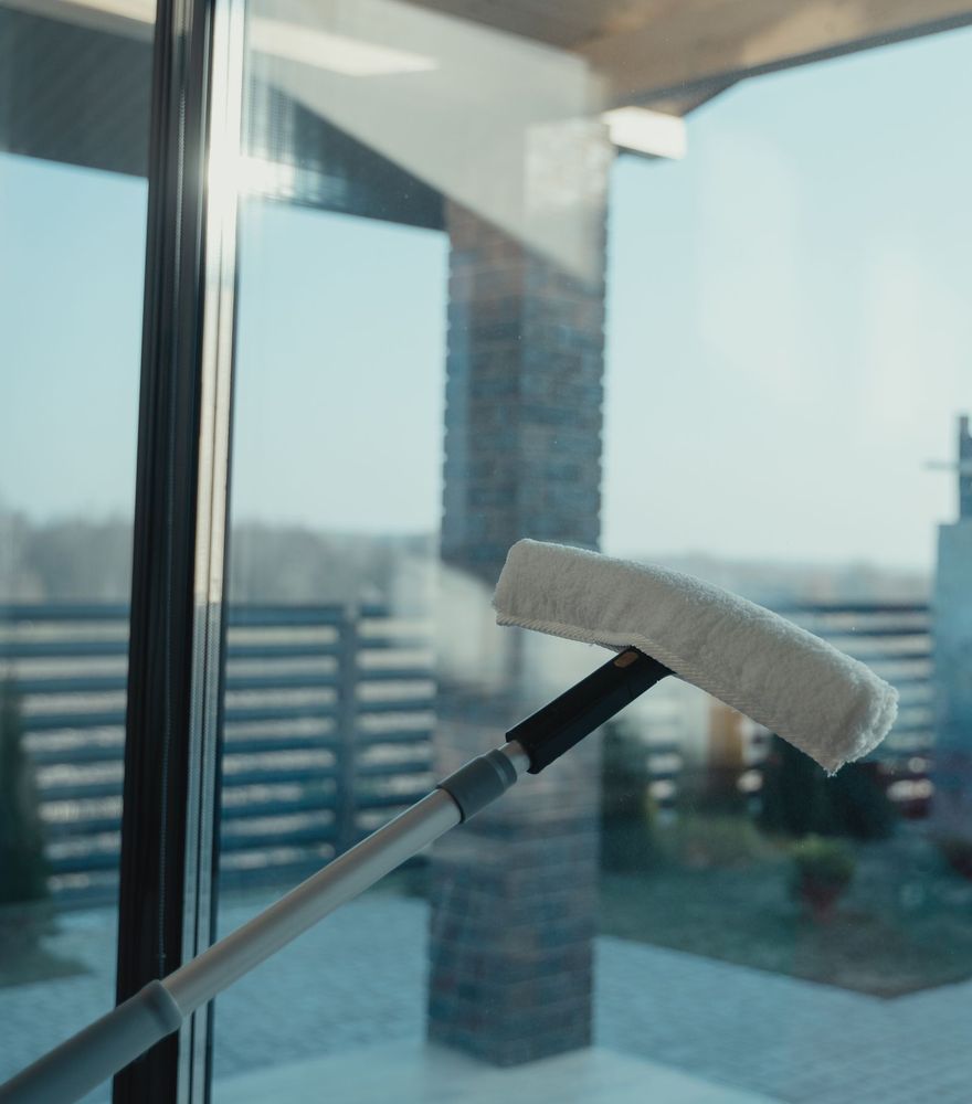 A soft water-fed brush sweeping across a tall pane of glass, the frame gleaming behind it